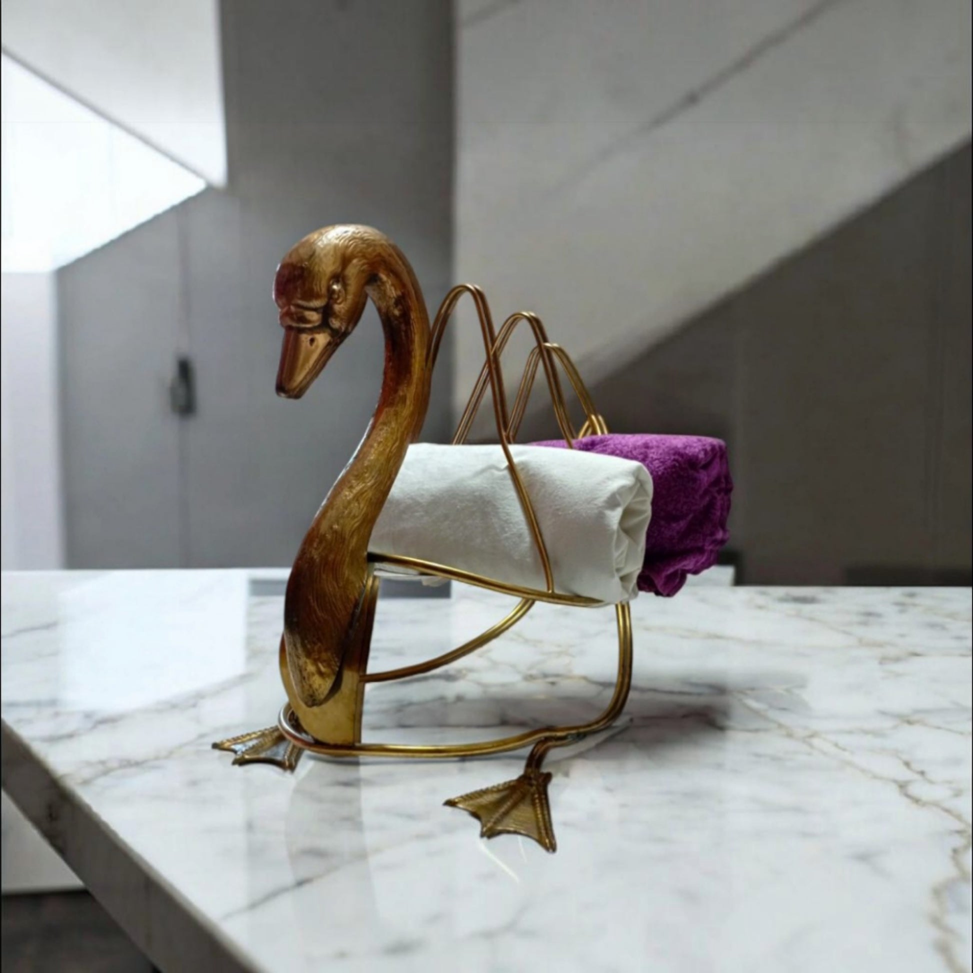 Vintage swan magazine rack in brass-toned metal styled in a bathroom with folded white and purple towels.