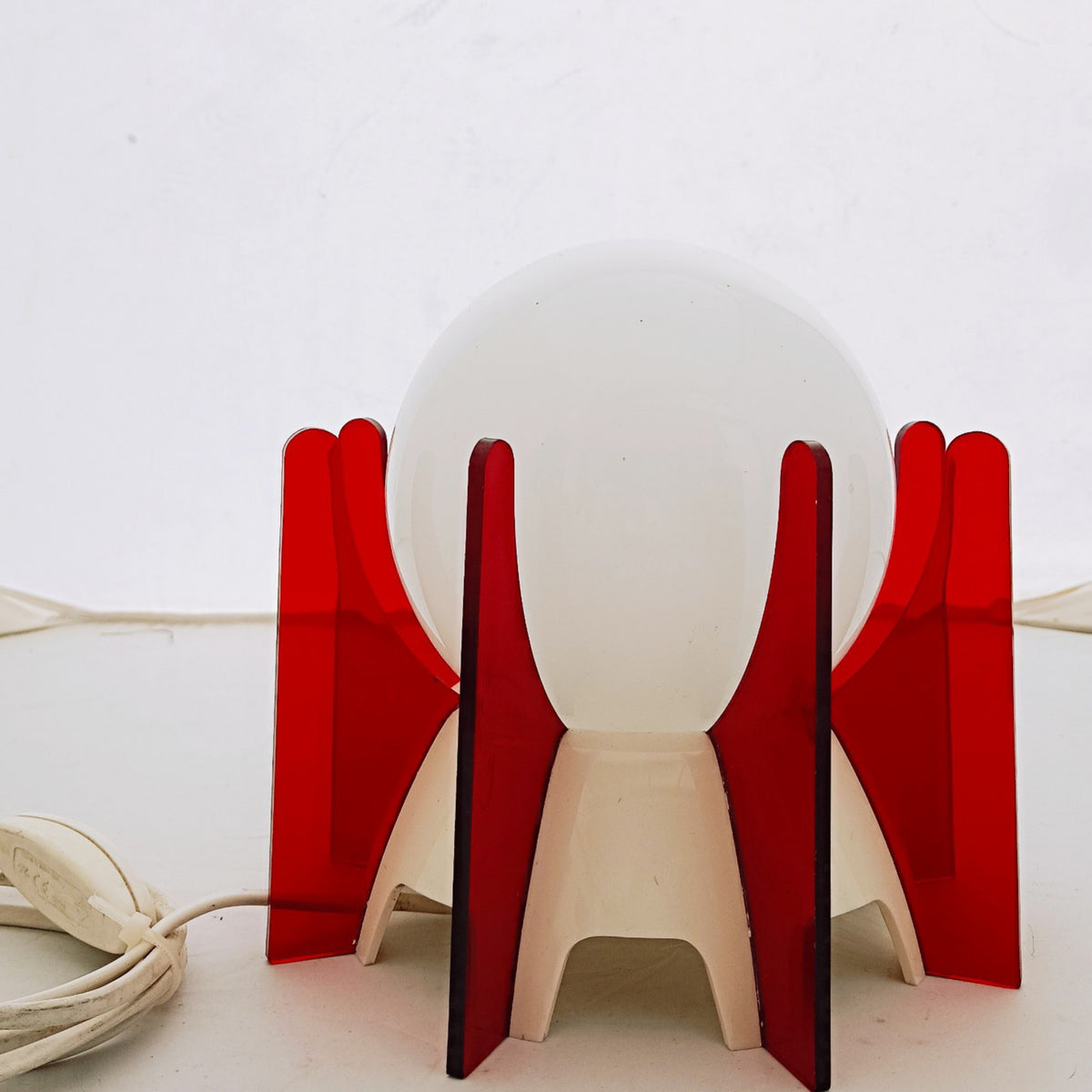 White glass globe held within translucent red panels and white supports